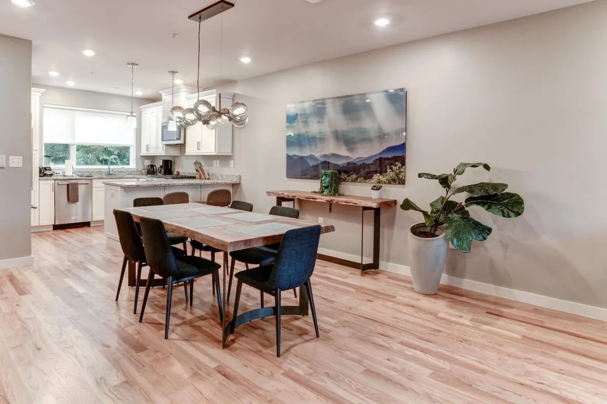 An inviting dining area adjacent to a sleek kitchen, with a dining table ready for shared meals, vibrant wall art, and touches of greenery that create a welcoming atmosphere for group dining or celebration.