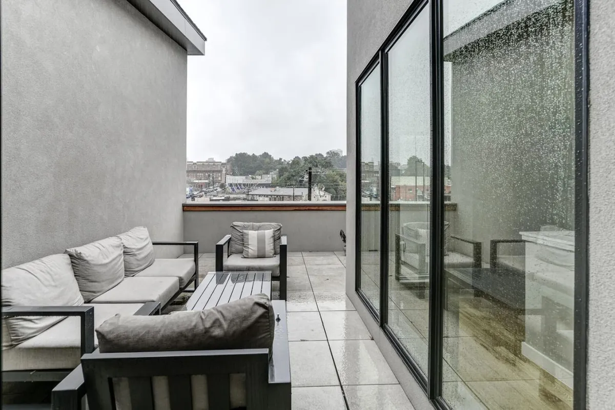 This image shows a serene outdoor seating area with comfortable chairs positioned to take in panoramic city views. The space features large glass windows that visually connect the rooftop patio to the urban landscape below, enhancing the sense of elevation and exclusivity. The mood is tranquil, inviting relaxation and socialization against the backdrop of Asheville’s skyline.