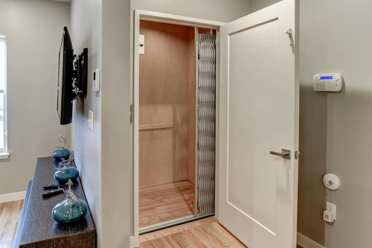 A contemporary elevator entrance seen within a living space, with the elevator doors open. A television and decorative vases are nearby, showcasing how the elevator is seamlessly integrated into everyday living areas.
