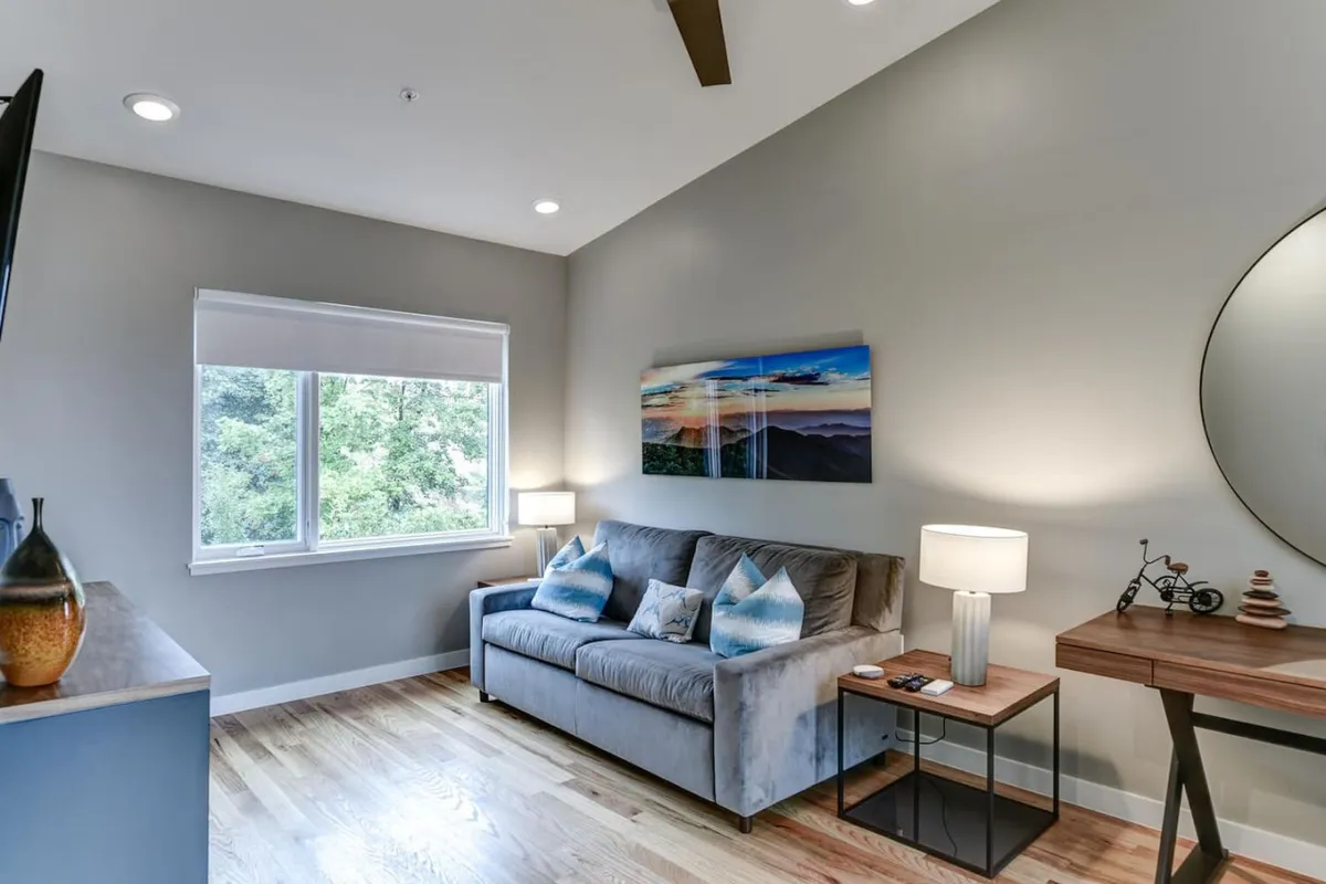 A cozy living area with a comfortable sofa positioned near a window overlooking the outside, accented by tasteful wall art and a side table with a lamp. The mood is welcoming and relaxing, ideal for recounting a day spent in the city.