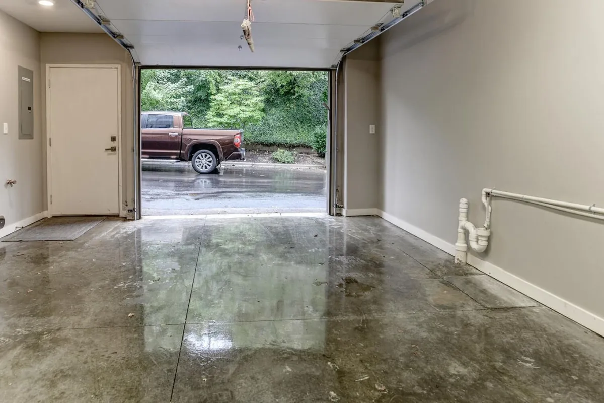 A clean, organized garage featuring a visible garage door, polished concrete floor, and wall-mounted utilities. The space is clearly designed for parking vehicles with additional room for storage and practical home organization.