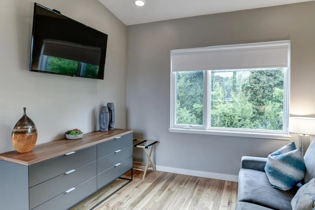 A modern, cozy living-dining area with a television, window offering city views, dining table, and decorative vase. The space feels welcoming, with ample room for relaxing and entertaining, and the window hints at the home's connection to the surrounding urban environment.