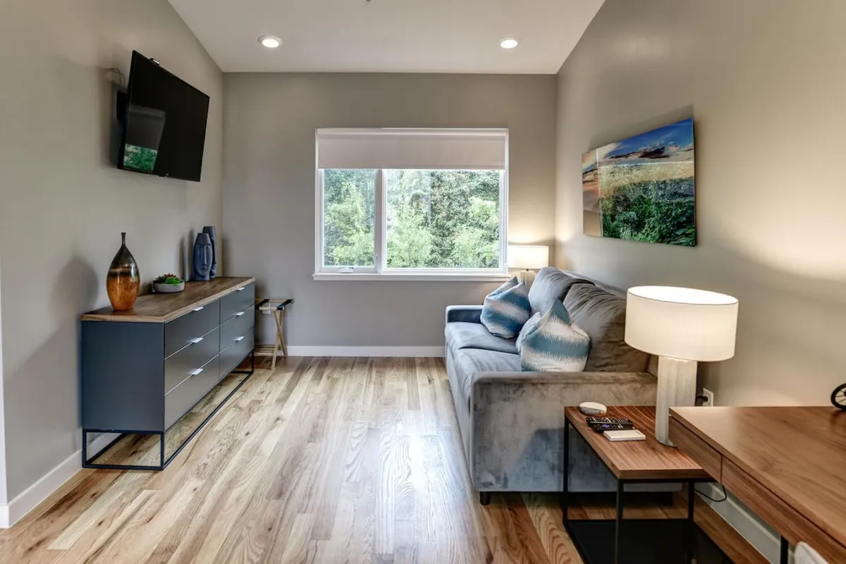 A cozy lounge featuring a plush sofa, a window with city views, tasteful wall art, a stylish lamp, and a side table—creating a comfortable environment for unwinding or informal conversations after a busy day.