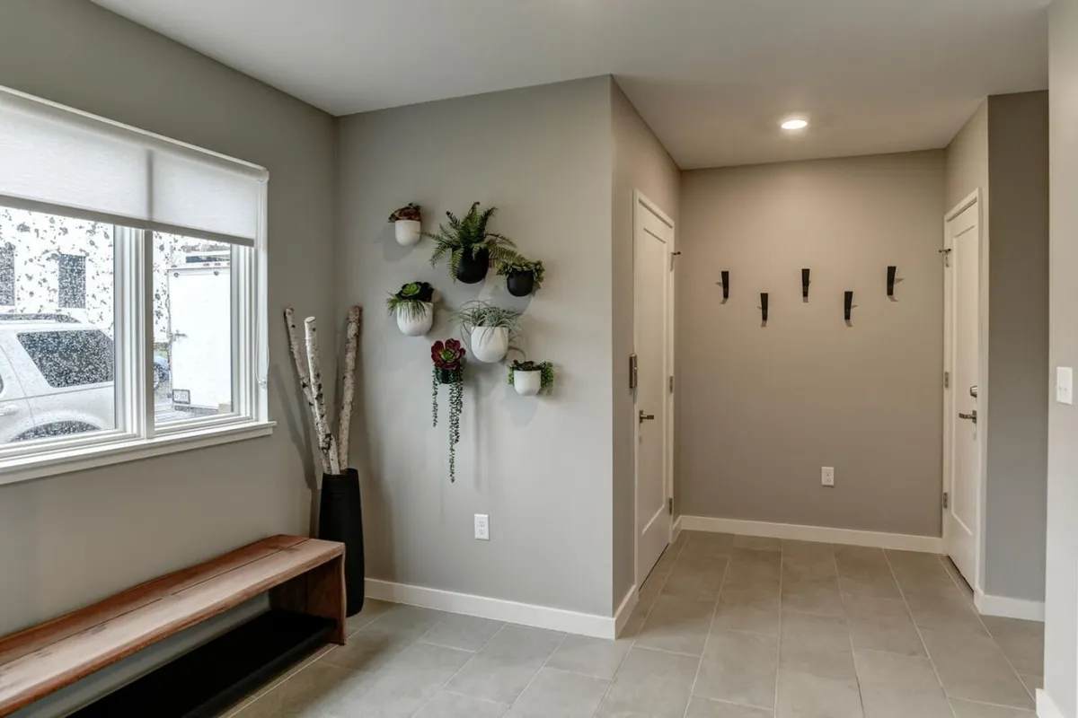 This image features a welcoming entryway flushed with natural light from a window, accented by a vertical plant wall and a wooden bench. The space feels calm and inviting, suggesting an immediate sense of arrival and connection to the vibrant surroundings just outside the door.