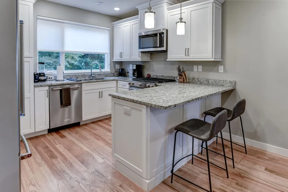 A contemporary kitchen with granite countertops, sleek modern appliances, and bar stools arranged for casual dining or informal meetings. The layout is welcoming for entertaining, quick meals, or collaborative discussion over coffee.