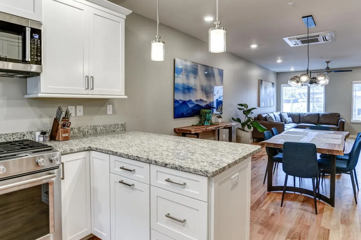 An open-concept space that elegantly combines the kitchen, dining, and living areas, with a granite countertop, stainless steel appliances, a cozy sofa, and eye-catching art. The setup is ideal for seamless entertaining and larger group interactions.